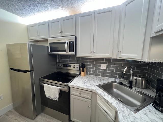 kitchen featuring white cabinets, a sink, light stone countertops, tasteful backsplash, and appliances with stainless steel finishes