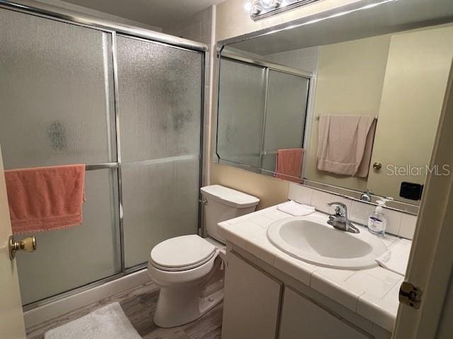 bathroom featuring vanity, toilet, a shower with shower door, and wood finished floors