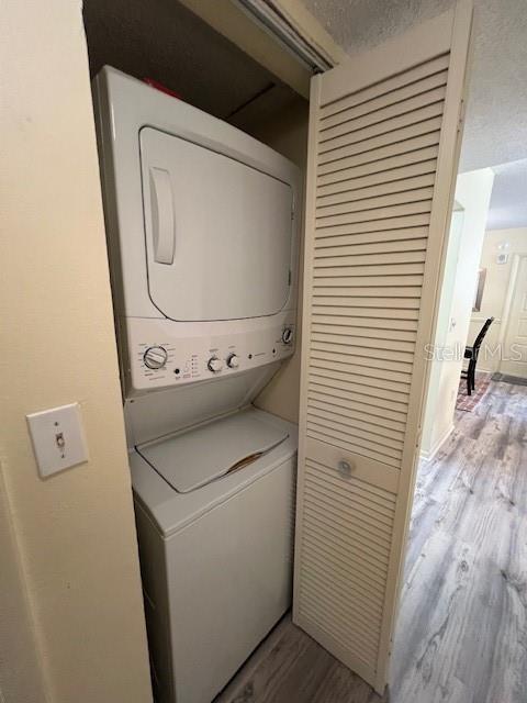 laundry room featuring wood finished floors, stacked washing maching and dryer, and laundry area