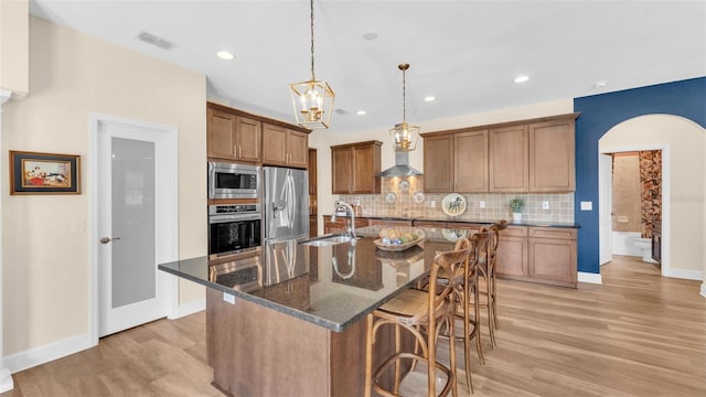 6372 English Creek Dr, Lakeland, FL 33811 - kitchen featuring appliances with stainless steel finishes, a kitchen bar, light wood-type flooring, backsplash, and arched walkways