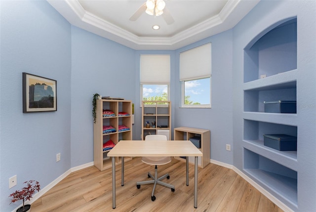 office with a tray ceiling, ceiling fan, light wood-style floors, built in shelves, and ornamental molding