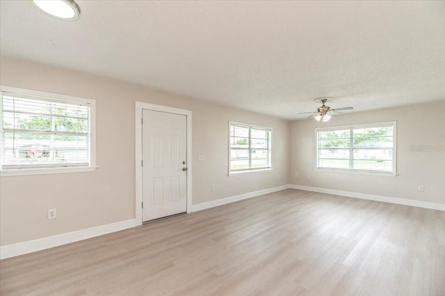 empty room featuring a textured ceiling, baseboards, light wood-type flooring, and a ceiling fan