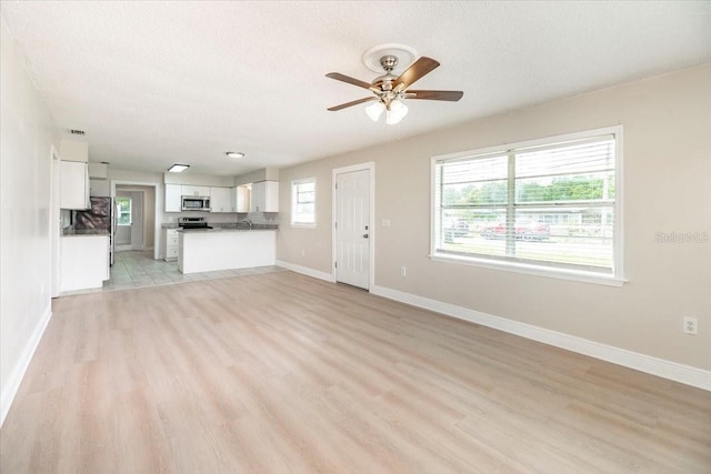 unfurnished living room with light wood-style flooring, a textured ceiling, ceiling fan, and baseboards