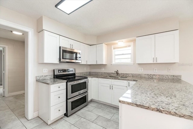 kitchen featuring appliances with stainless steel finishes, a sink, white cabinetry, and light stone countertops