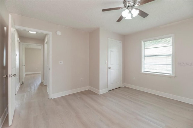 unfurnished bedroom featuring light wood-style flooring, baseboards, a textured ceiling, and a ceiling fan