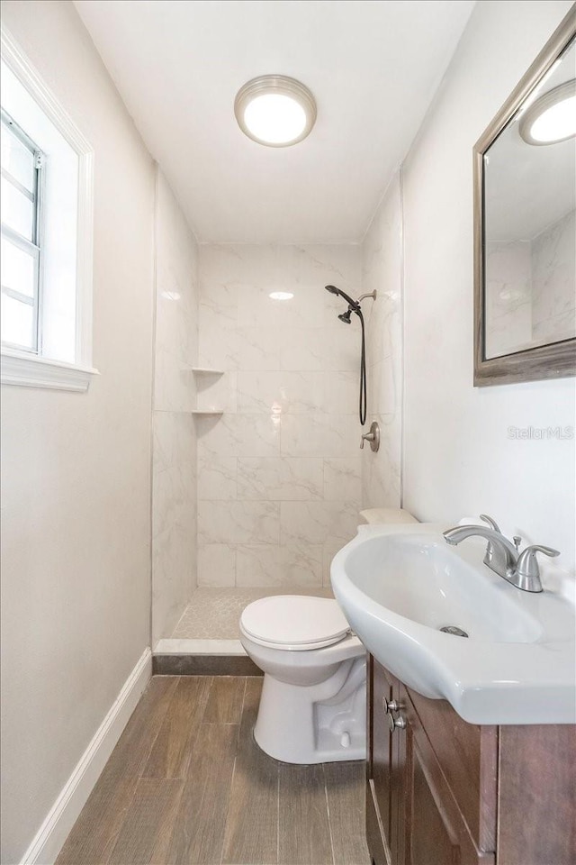 bathroom with baseboards, toilet, wood finish floors, vanity, and tiled shower