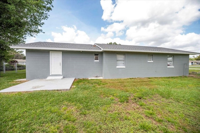 rear view of house with a yard, concrete block siding, a patio area, and fence