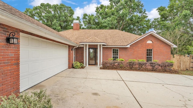 ranch-style home with a shingled roof, an attached garage, a chimney, concrete driveway, and brick siding