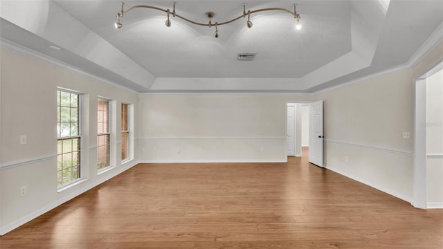 unfurnished room featuring ornamental molding, a tray ceiling, wood finished floors, and visible vents