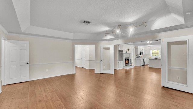 unfurnished living room featuring baseboards, a textured ceiling, light wood-style floors, a tray ceiling, and visible vents