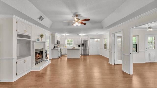 living area with a tiled fireplace, ceiling fan with notable chandelier, wood finished floors, and a raised ceiling