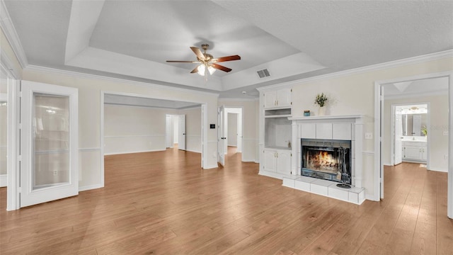 unfurnished living room with light wood-type flooring, a fireplace, a ceiling fan, crown molding, and a raised ceiling