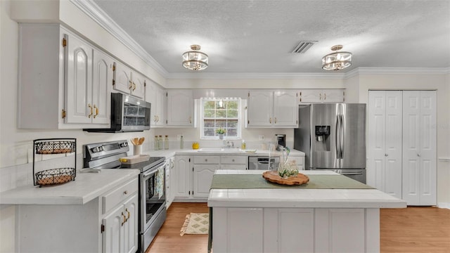 kitchen featuring tile counters, appliances with stainless steel finishes, visible vents, and light wood finished floors