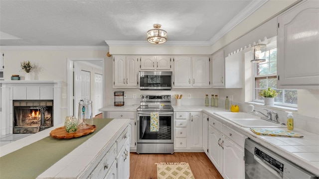 kitchen with tile counters, a fireplace, crown molding, appliances with stainless steel finishes, and a sink