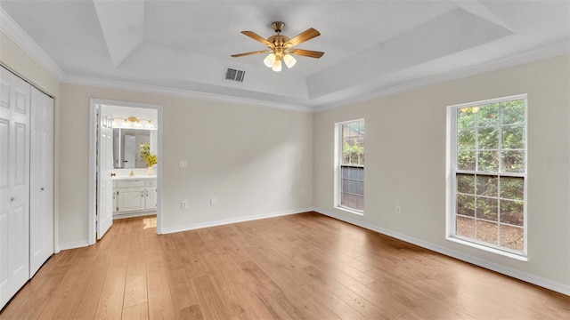 unfurnished bedroom with light wood-style floors, ensuite bathroom, visible vents, a raised ceiling, and baseboards
