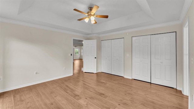 unfurnished bedroom with a tray ceiling, baseboards, two closets, and light wood-style floors