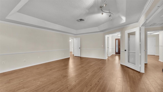 empty room featuring baseboards, a textured ceiling, visible vents, a tray ceiling, and hardwood / wood-style floors
