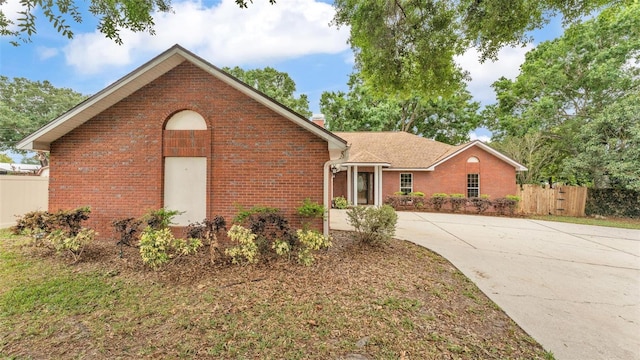 view of front of house featuring brick siding, fence, driveway, and a chimney