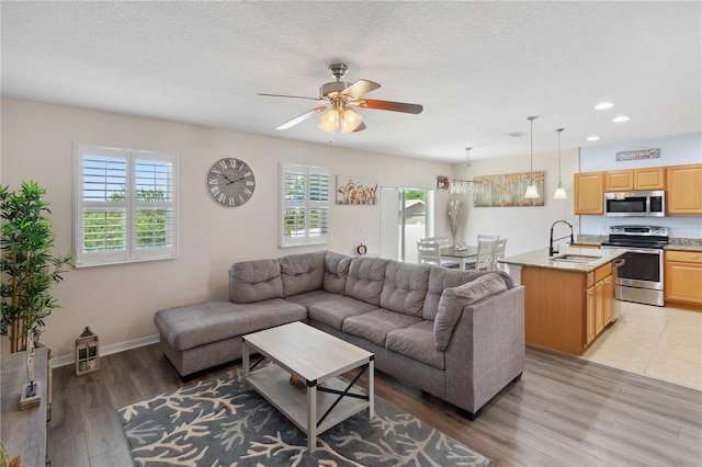living room featuring light wood-style floors, a textured ceiling, a ceiling fan, recessed lighting, and baseboards