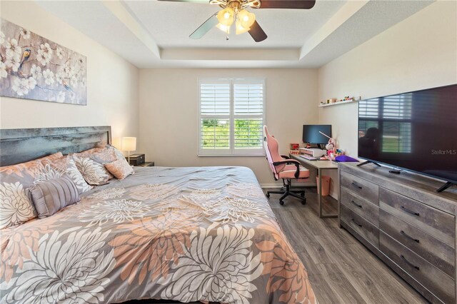 bedroom with ceiling fan, a raised ceiling, and wood finished floors