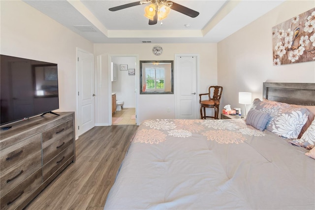bedroom featuring visible vents, wood finished floors, connected bathroom, and a raised ceiling