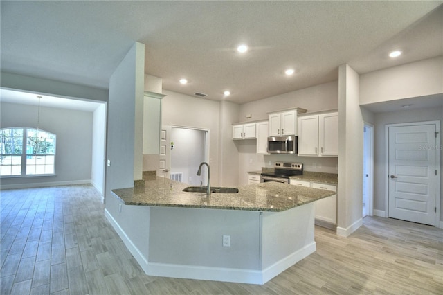 kitchen featuring a peninsula, light stone countertops, appliances with stainless steel finishes, a sink, and light wood-type flooring