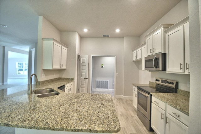 kitchen featuring visible vents, a peninsula, light stone countertops, stainless steel appliances, and a sink