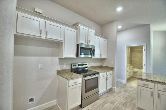 kitchen with white cabinets, light wood-style floors, light stone countertops, and appliances with stainless steel finishes