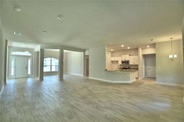 unfurnished living room featuring baseboards, a chandelier, a sink, visible vents, and light wood-style flooring