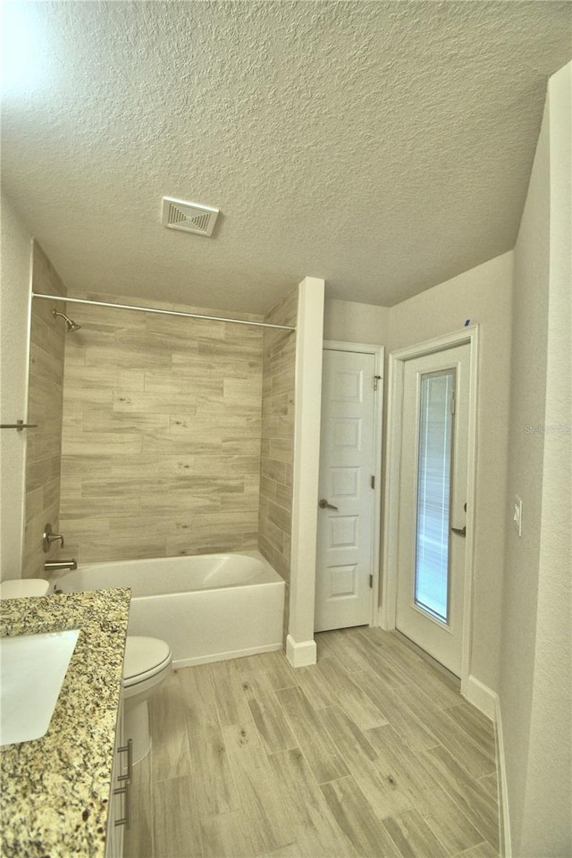 bathroom featuring toilet, bathing tub / shower combination, a textured ceiling, visible vents, and wood finished floors