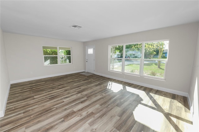unfurnished living room featuring visible vents, baseboards, and wood finished floors