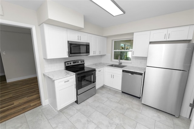 kitchen with appliances with stainless steel finishes, a sink, backsplash, and white cabinets
