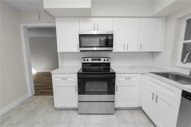 kitchen with baseboards, a sink, appliances with stainless steel finishes, white cabinetry, and backsplash