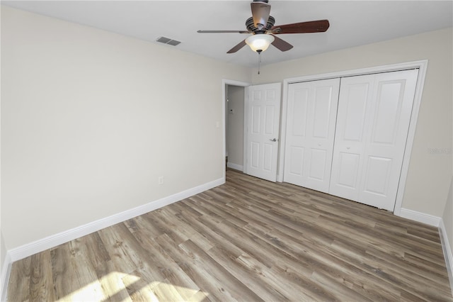 unfurnished bedroom with wood finished floors, baseboards, a closet, and visible vents