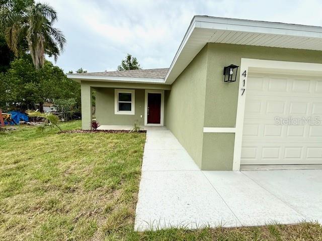 doorway to property featuring concrete driveway, a lawn, a garage, and stucco siding