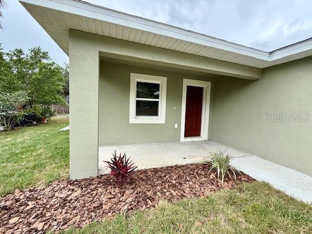 view of exterior entry featuring a lawn and stucco siding