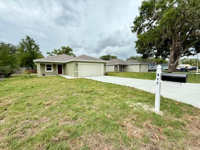 ranch-style home featuring stucco siding, fence, a front lawn, an attached garage, and driveway