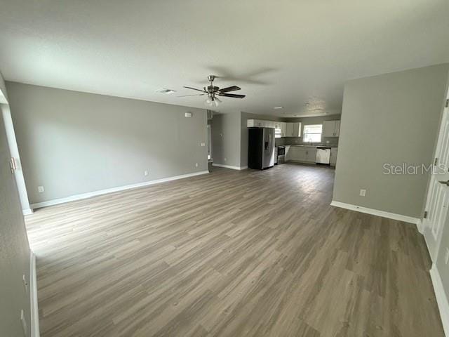 unfurnished living room featuring wood finished floors, ceiling fan, and baseboards