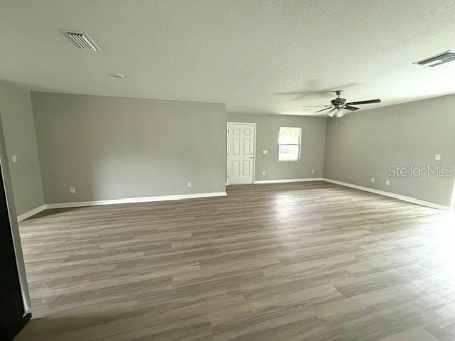 spare room with a textured ceiling, wood finished floors, ceiling fan, and visible vents
