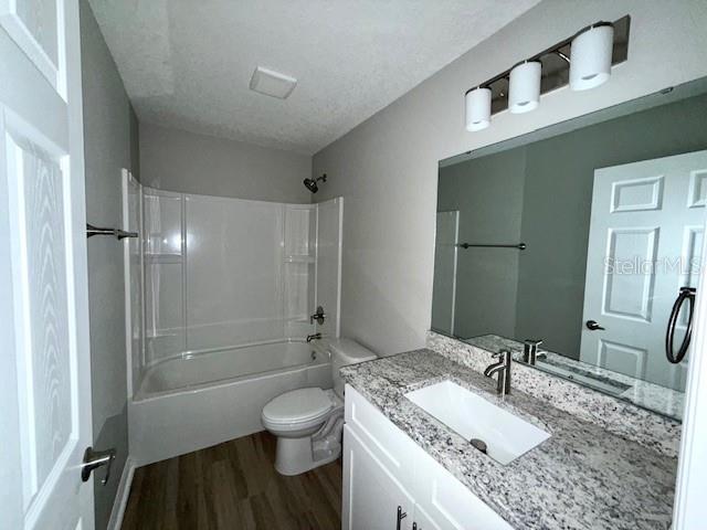 full bathroom with vanity, shower / tub combination, a textured ceiling, toilet, and wood finished floors