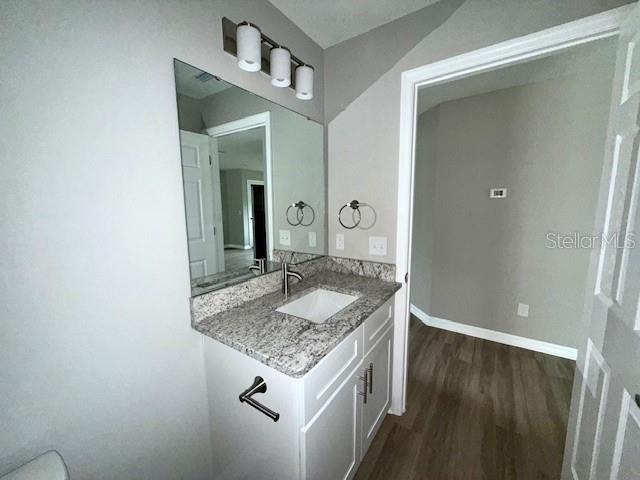half bath with baseboards, vanity, and wood finished floors