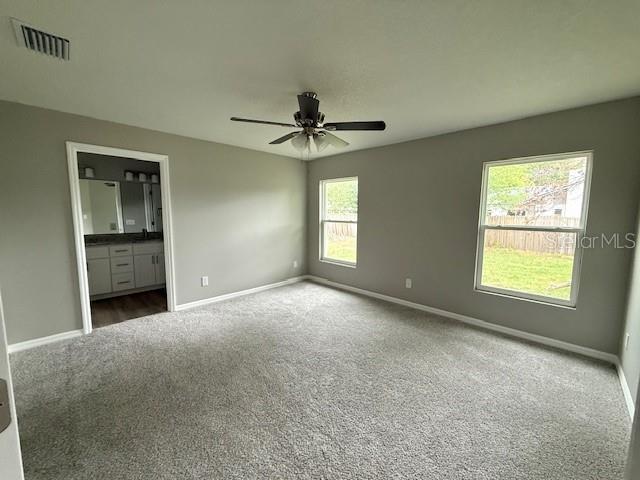 unfurnished bedroom with visible vents, baseboards, dark carpet, a ceiling fan, and connected bathroom