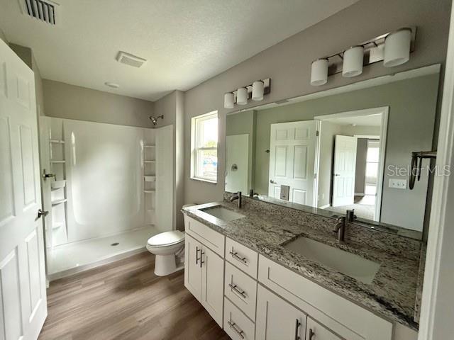 bathroom with toilet, a sink, visible vents, and walk in shower