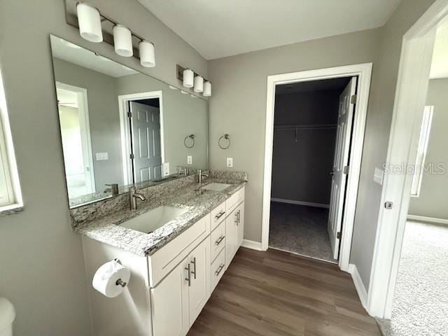 bathroom with double vanity, baseboards, a sink, and wood finished floors