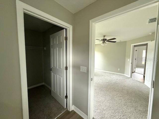 hallway with dark carpet, baseboards, and visible vents