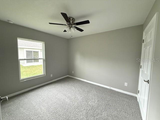 carpeted spare room featuring baseboards and ceiling fan