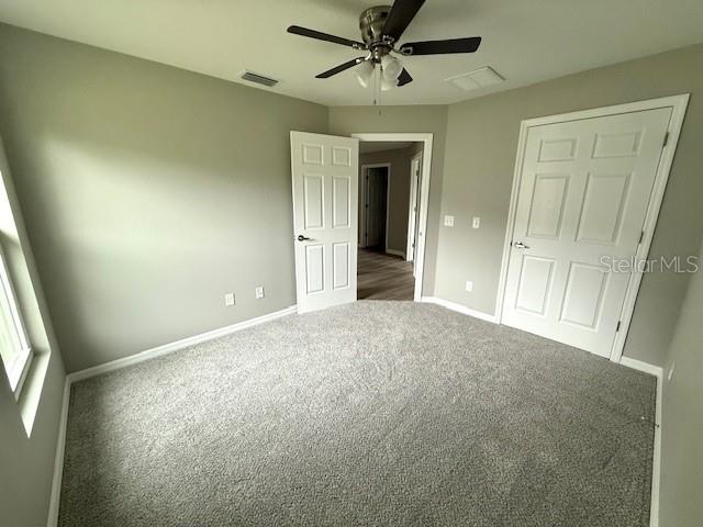 unfurnished bedroom featuring carpet, visible vents, baseboards, and a ceiling fan
