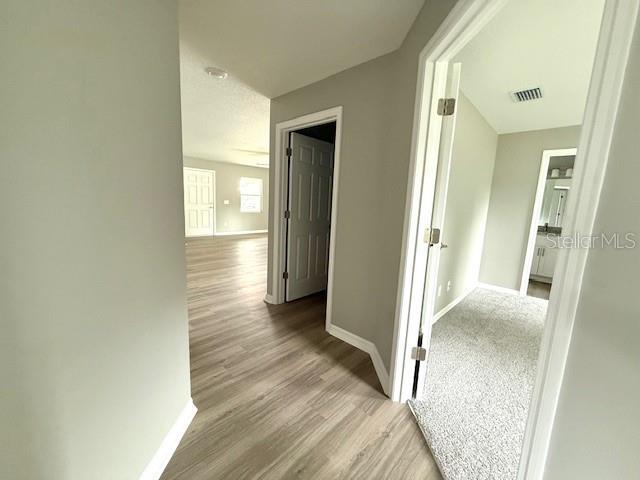 hall featuring wood finished floors, baseboards, and visible vents