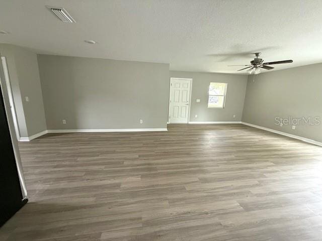 empty room with a textured ceiling, a ceiling fan, visible vents, wood finished floors, and baseboards