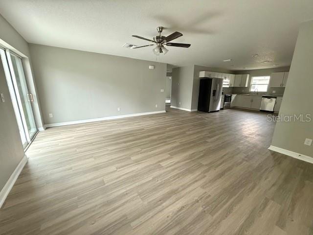 unfurnished living room with ceiling fan, wood finished floors, and baseboards